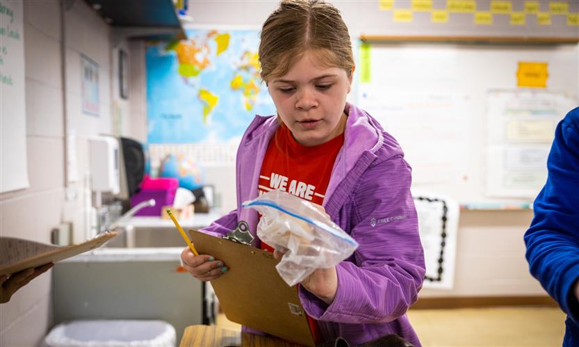 A girl wearing a purple jacket picks up a plastic bag